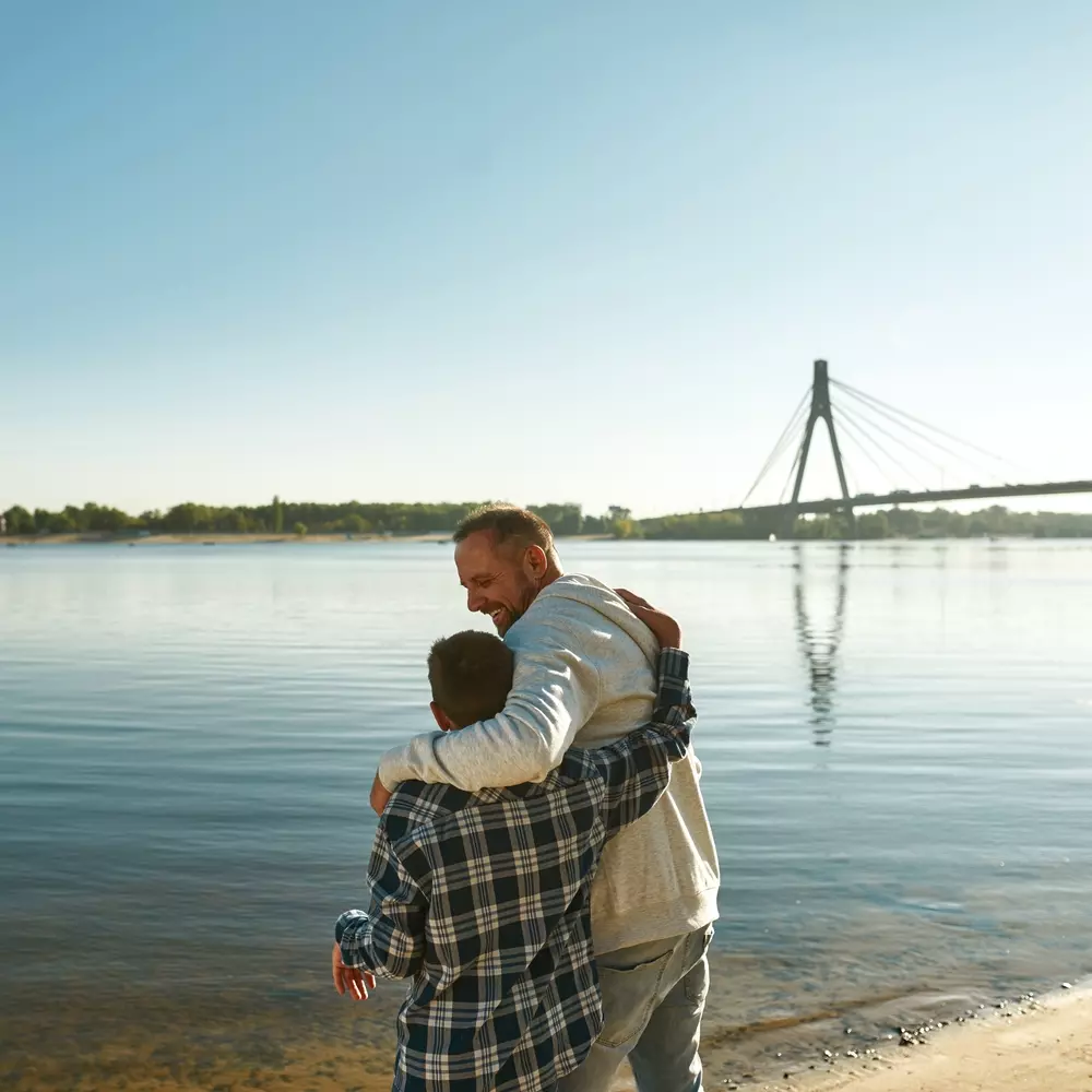 Padre e hijo con discapacidad abrazándose por la espalda delante de un lago